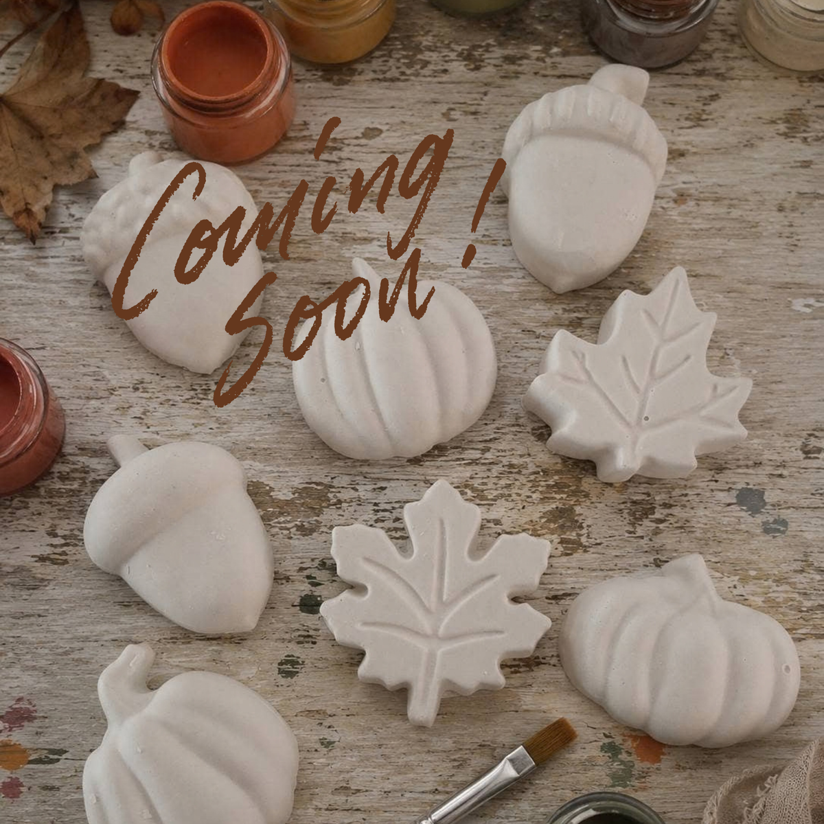 White plaster fall-themed decorative pieces, including pumpkins, acorns, and maple leaves, arranged on a rustic wooden surface with paint jars and a paintbrush.