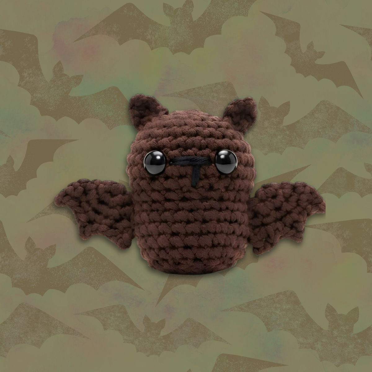 A brown crocheted bat plush toy with large black eyes, a black stitched nose, and small wings, centered against a muted olive-green background with a faint bat pattern.