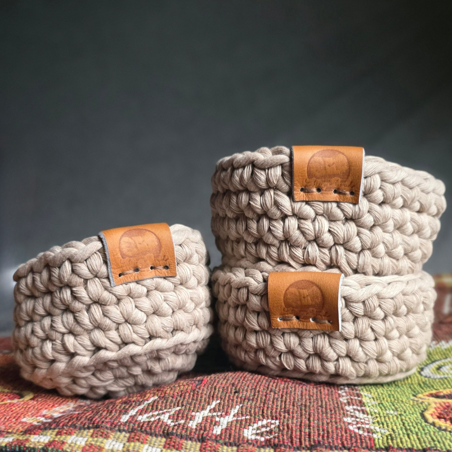 Set of three hand-crocheted nesting baskets in light gray yarn, featuring small brown faux-leather labels on the rims.